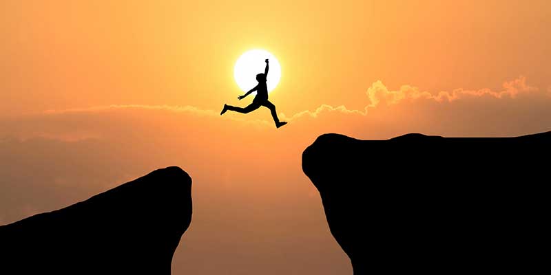 Man leaping from one cliff to another at sunset