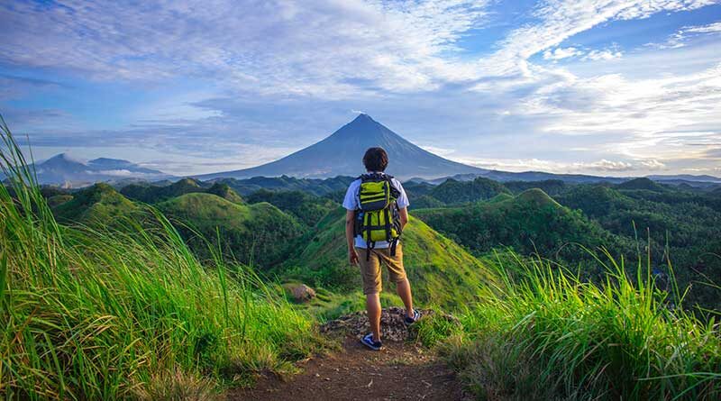 Boy with backpack looking up at mountain