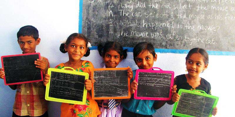 Children standing in front of blackboard with their slates