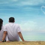 Couple on a beach looking at a heart sign in the clouds