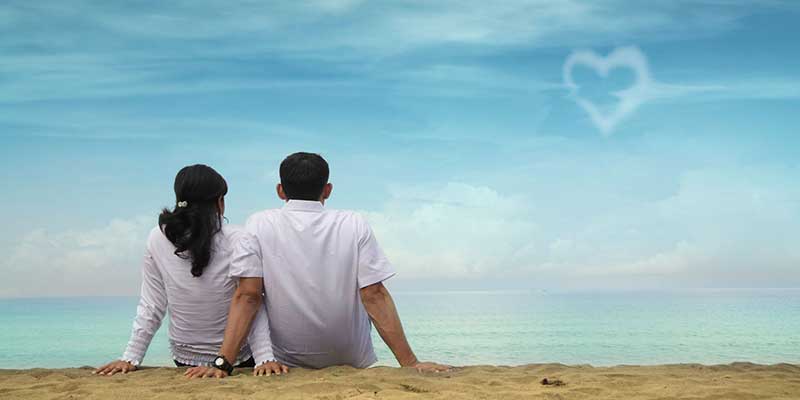 Couple on a beach looking at a heart sign in the clouds