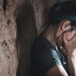 Depressed girl leaning against a wall and covering her face