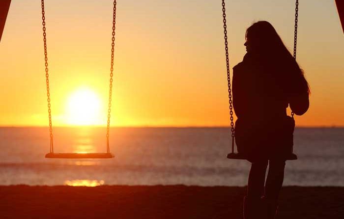 Girl sitting on a swing at sunset with an empty swing beside her