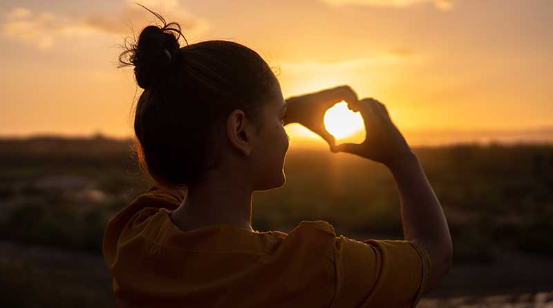 Girl making a heart shape with hands at sunset
