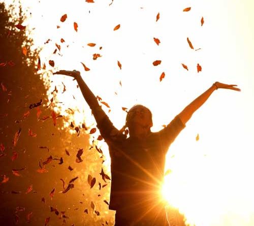 Girl throwing leaves into the air at sunset