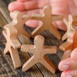 Hands cupped around six wooden figures in a circle