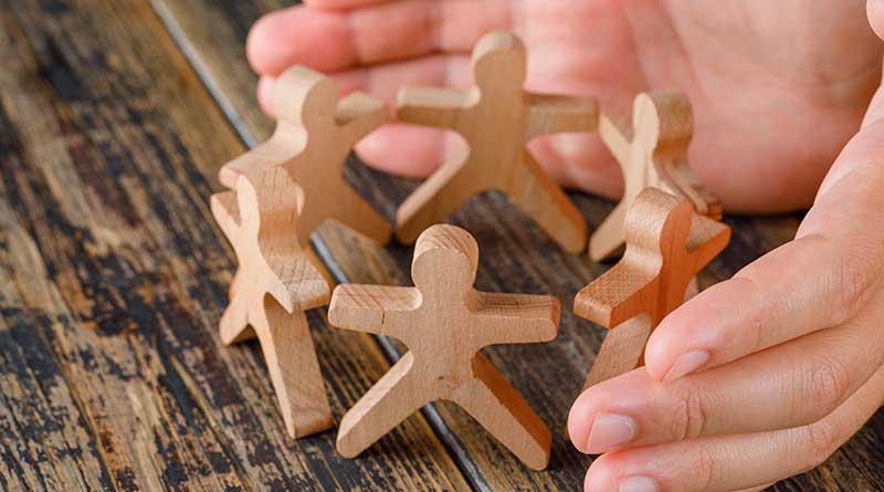 Hands cupped around six wooden figures in a circle