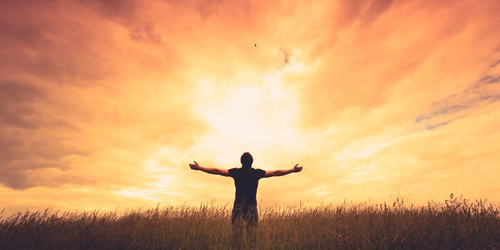 Man standing in a field at sunset and raising his arms to the sky
