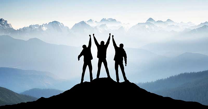 Mountain climbers standing at the top of a mountain with arms raised in victory