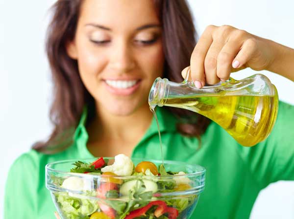 Young woman pouring oil onto salad