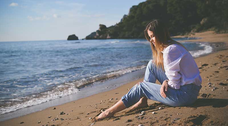 Sad, pensive young woman sitting on a beach