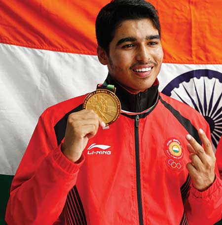 Saurabh Chaudhary holding up his gold medal in front of the Indian tricolour