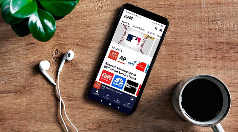 Smartphone with TuneIn Radio app on-screen on a table near coffee cup and potted plant