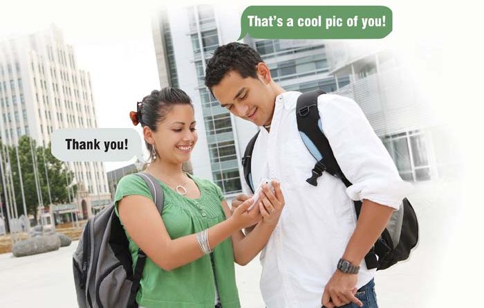 Two students looking at smartphone; one compliments the other who thanks him