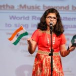 Sumitha Satish on stage singing while holding the flags of India and UAE