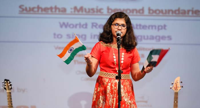 Sumitha Satish on stage singing while holding the flags of India and UAE