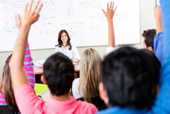 Teacher smiling at students raising their hands