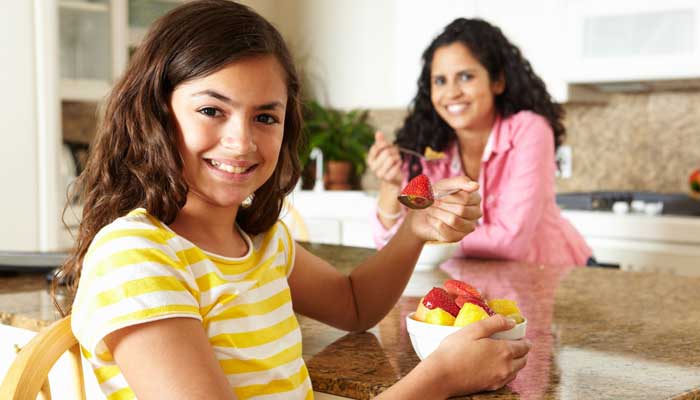 Teen girl having breakfast in the kitchen with her mother