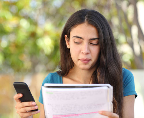 Teenage student looking sideways at mobile phone while studying