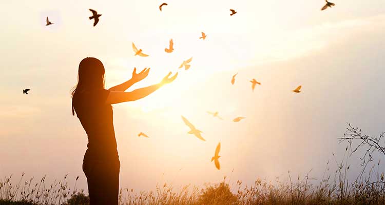 Woman standing with her arms outstretched at sunset with birds flying around