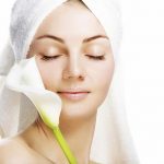 Woman wearing a towel over her hair placing a flower against her facial skin