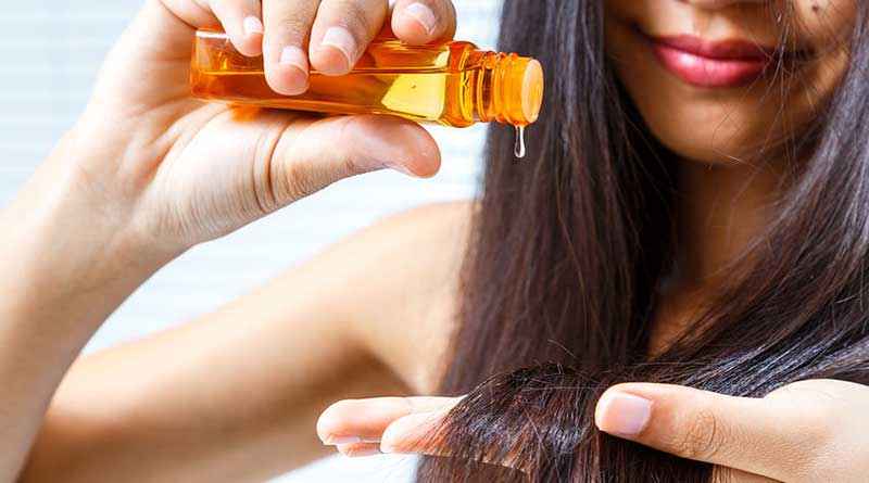 Woman pouring oil from bottle onto her hair