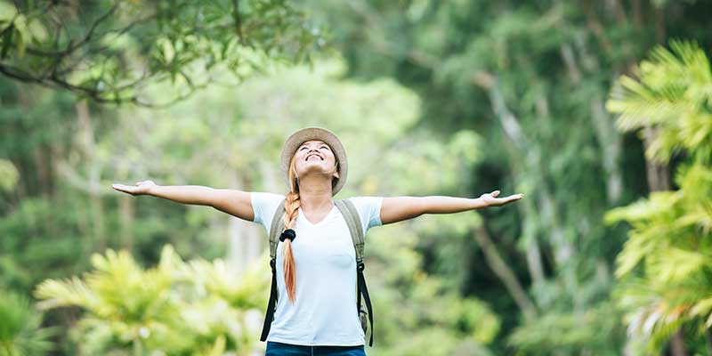 Young happy woman with arms raised in gratitude enjoying nature