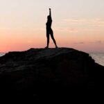 Young woman with raised arm standing on top of a rock in the ocean