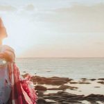 Young woman looking out at the sea with her arms outstretched.
