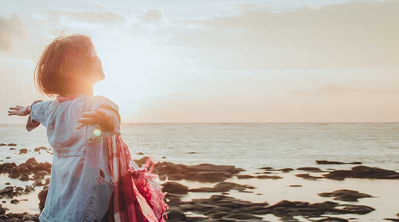 Young woman looking out at the sea with her arms outstretched.