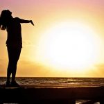 Young woman with her arms outstretched in acceptance at sunset