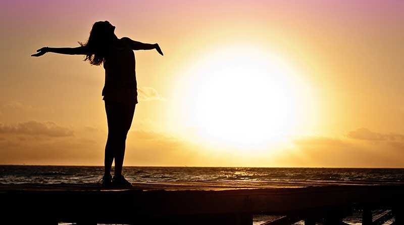 Young woman with her arms outstretched in acceptance at sunset