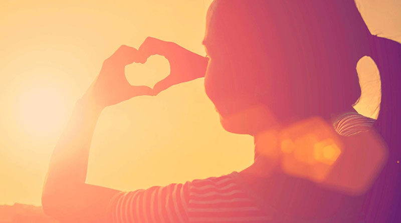 Young woman making heart shape with her hands at sunrise