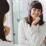 Young woman looking in the mirror at a heart shape drawn around her face