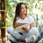 Young woman sitting outside in nature and writing in a journal
