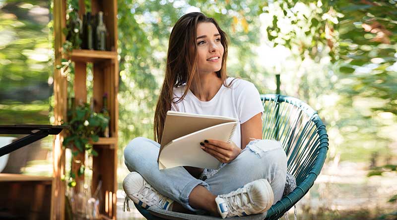 Young woman sitting outside in nature and writing in a journal