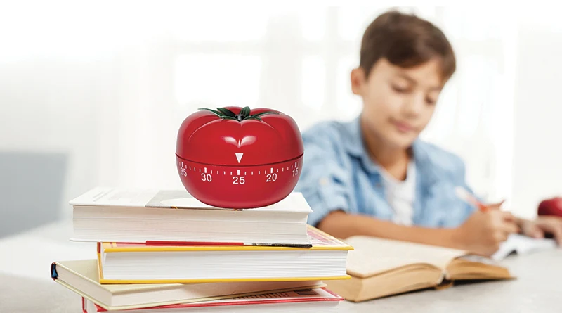 Boy studying at his desk with a pomodoro timer resting on top of his books.