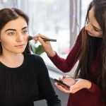 Female makeup artist applying blusher to a young female model