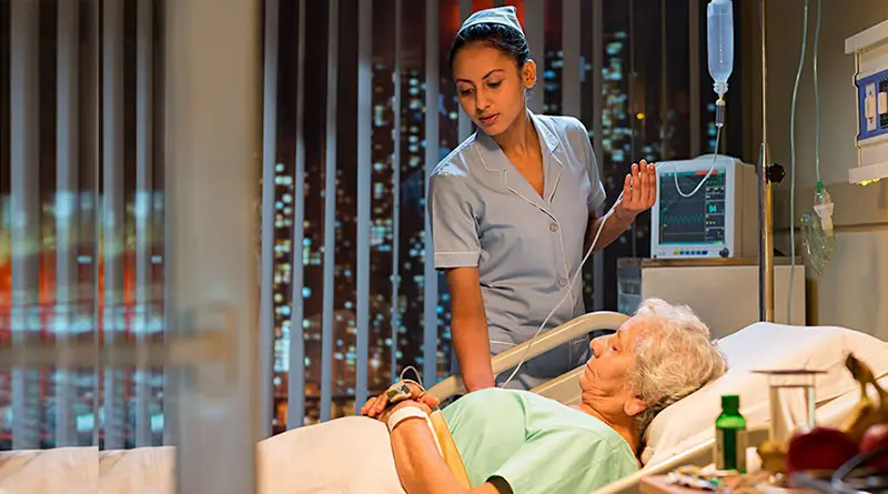 Young female nurse looking after old female patient lying in hospital bed.