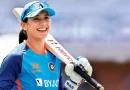 Smriti Mandhana holding a bat over her shoulder and smiling.