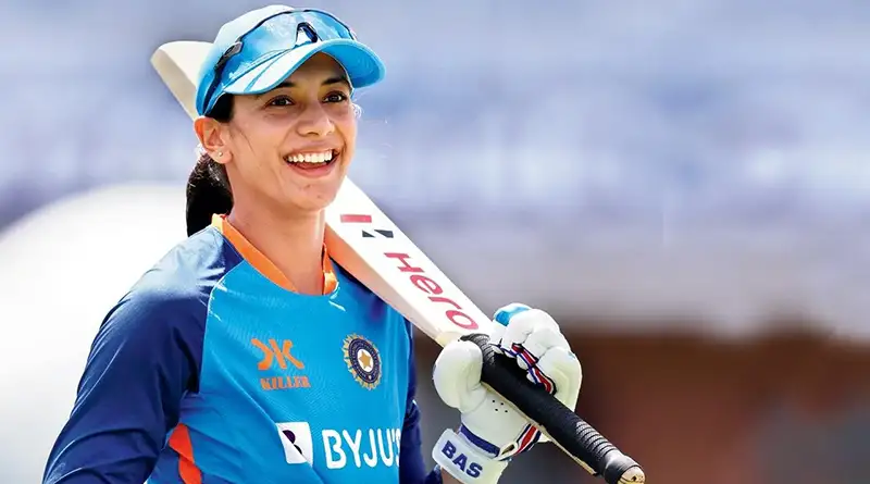 Smriti Mandhana holding a bat over her shoulder and smiling.