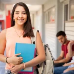 Young woman carrying books and a backpack and smiling